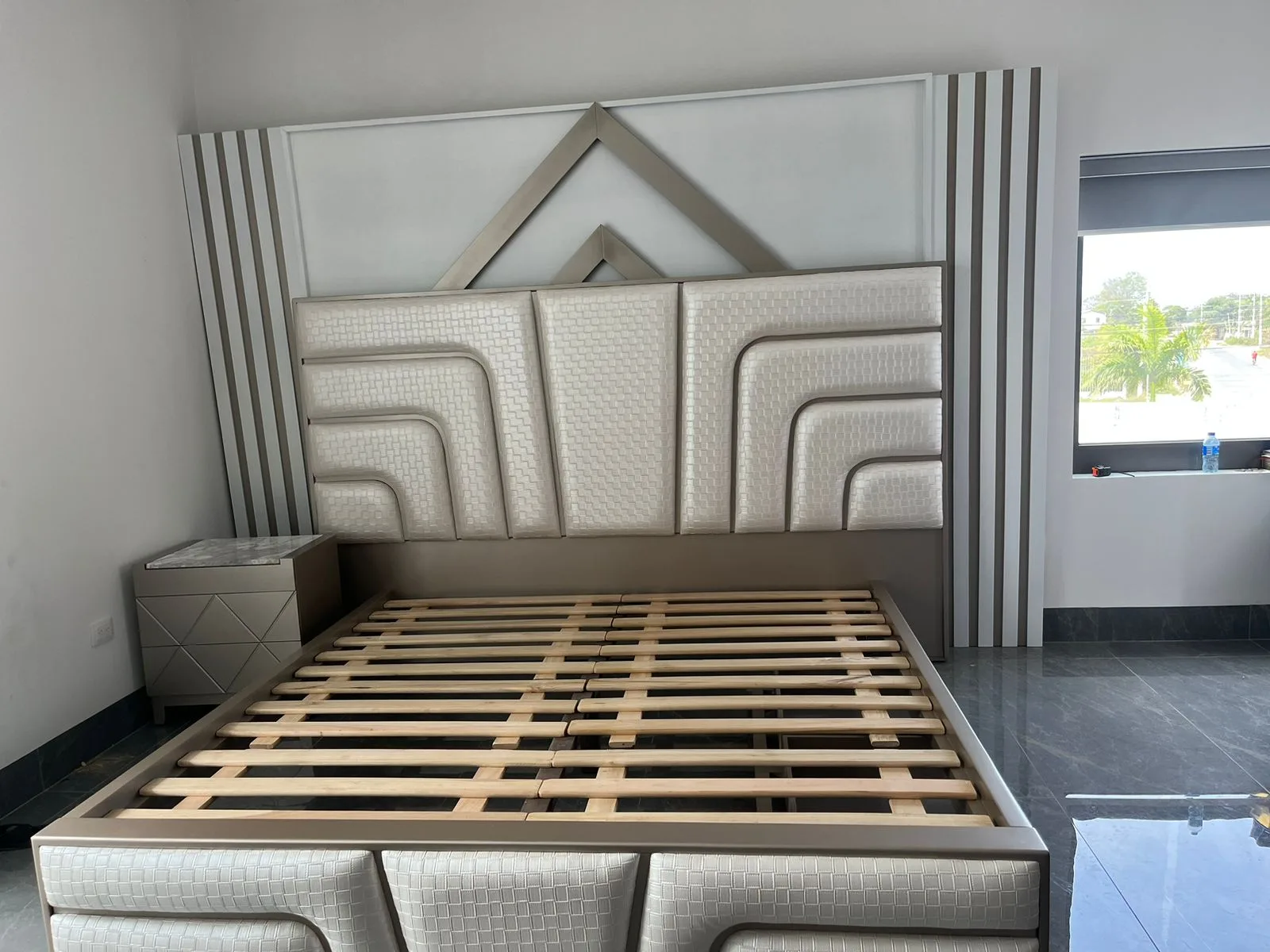 Cabecera de cama con textura tejida en canales curvos y remate metálico triangular (estilo art-decó)
